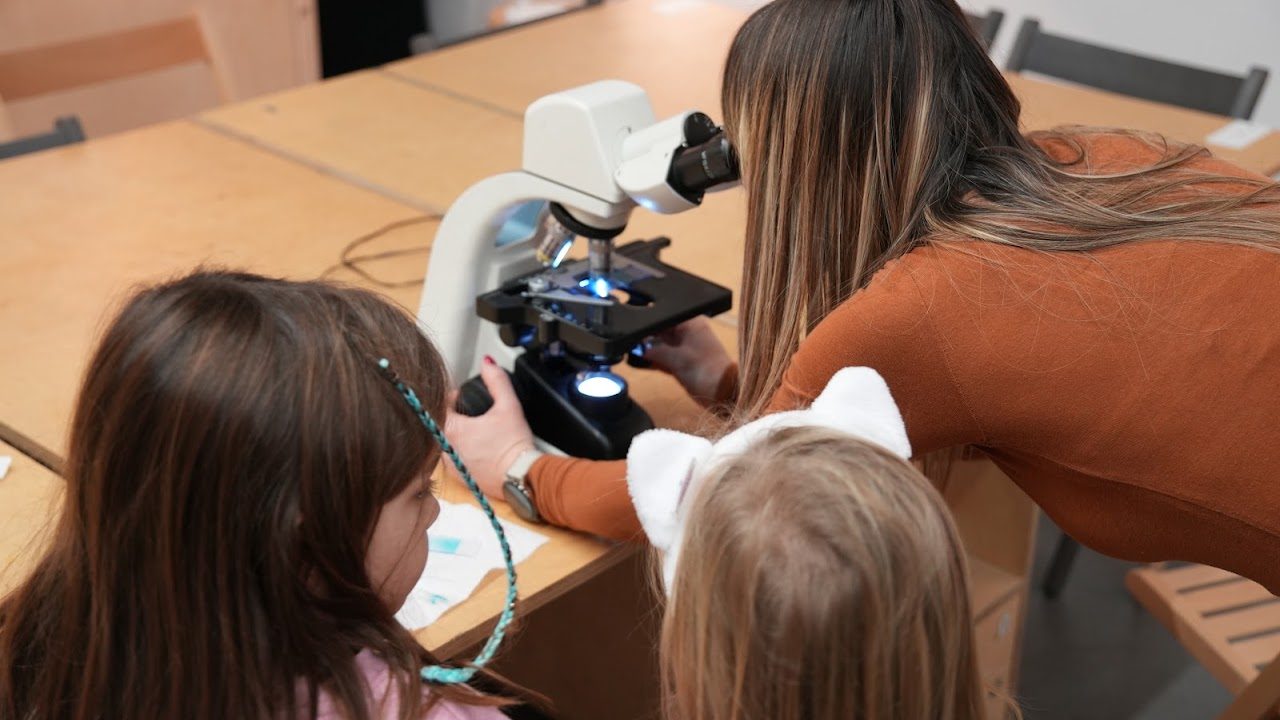 Edukatorka pokazuje deci uzorak pod mikroskopom